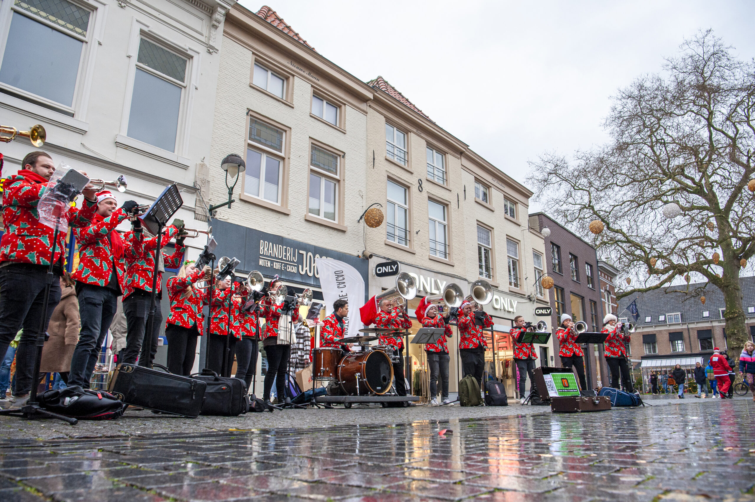 Muzikanten in kleurrijke kostuums spelen blaasinstrumenten in een levendig straatconcert op een geplaveide straat met omringende historische gebouwen en toeschouwers.