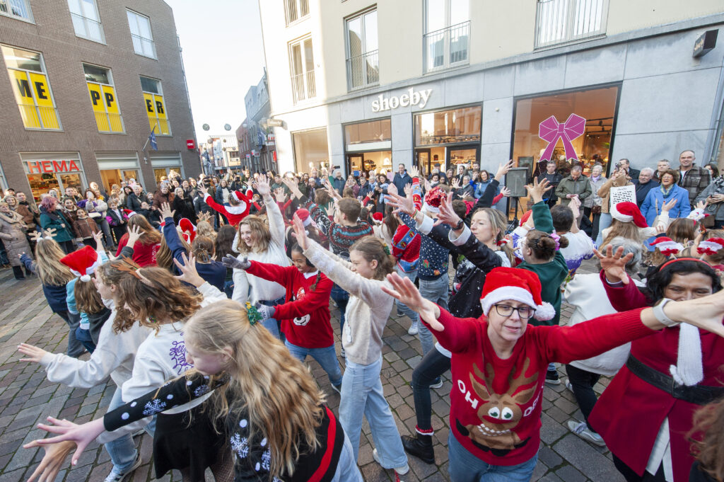 Groep mensen viert kerst in drukke winkelstraat met feestelijke kleding en kerstmutsen winkelgevels op achtergrond vreugdevolle sfeer op heldere dag