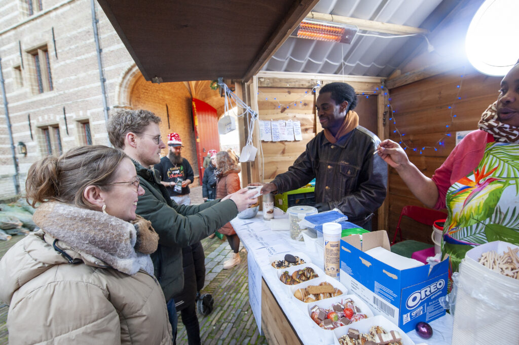 Mensen genieten van een straatmarkt in Nederland waar een kraampje diverse snacks aanbiedt en klanten worden bediend in een gezellige buitenomgeving.