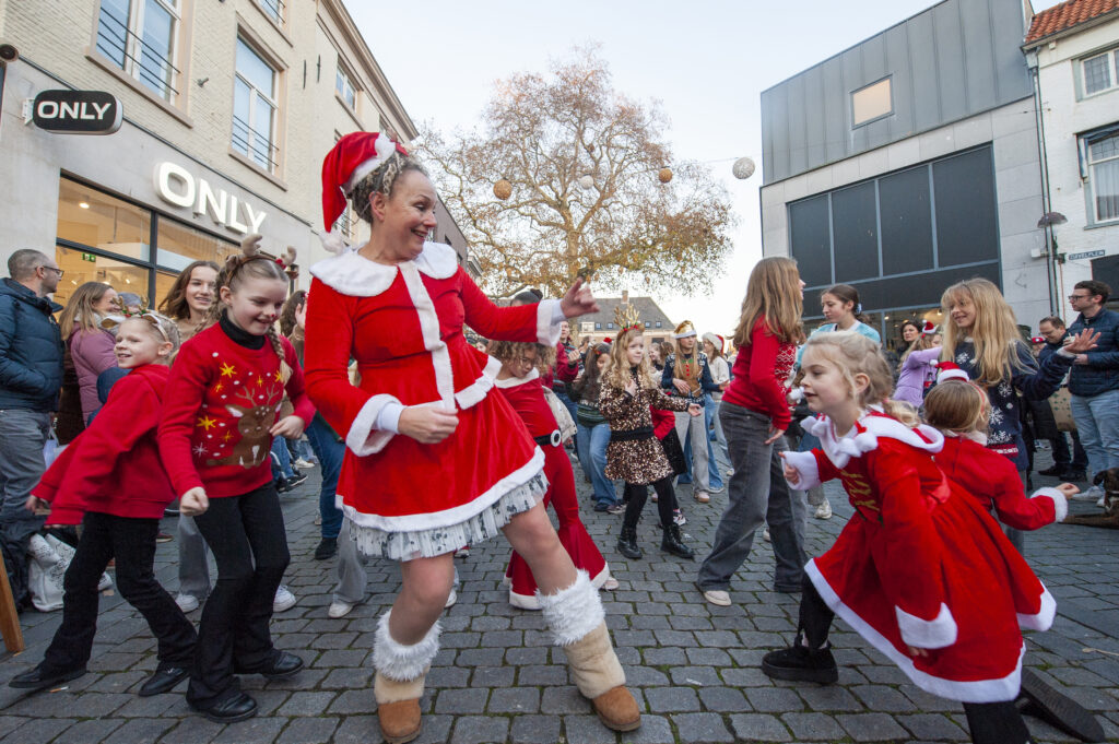Mensen vieren een feestelijke kerstparade in een drukke winkelstraat dansen in kerstkleding omgeven door blije menigte en winterse sfeer in een stad.