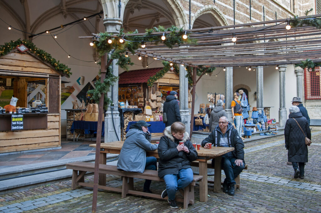 Mensen genieten van warme dranken op een gezellige kerstmarkt vol houten kraampjes in een historisch plein met feestelijke decoraties in de stad.