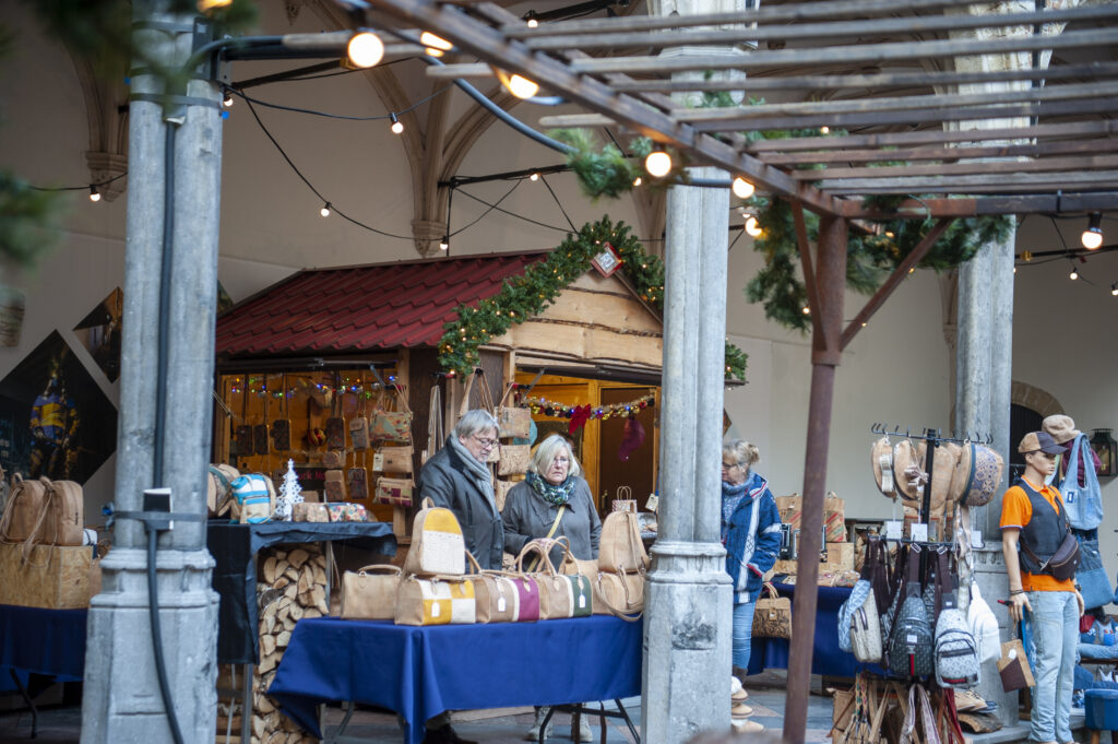 Kerstsfeer op een gezellige markt met diverse kraampjes onder sfeervolle lichtjes. Bezoekers bekijken handgemaakte producten en genieten van de feestelijke ambiance.