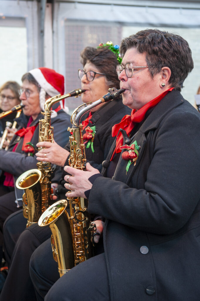Muzikanten spelen saxofoon tijdens een kerstconcert met feestelijke kleding en decoraties passend bij de kerstsfeer binnen een overdekte evenementenruimte.