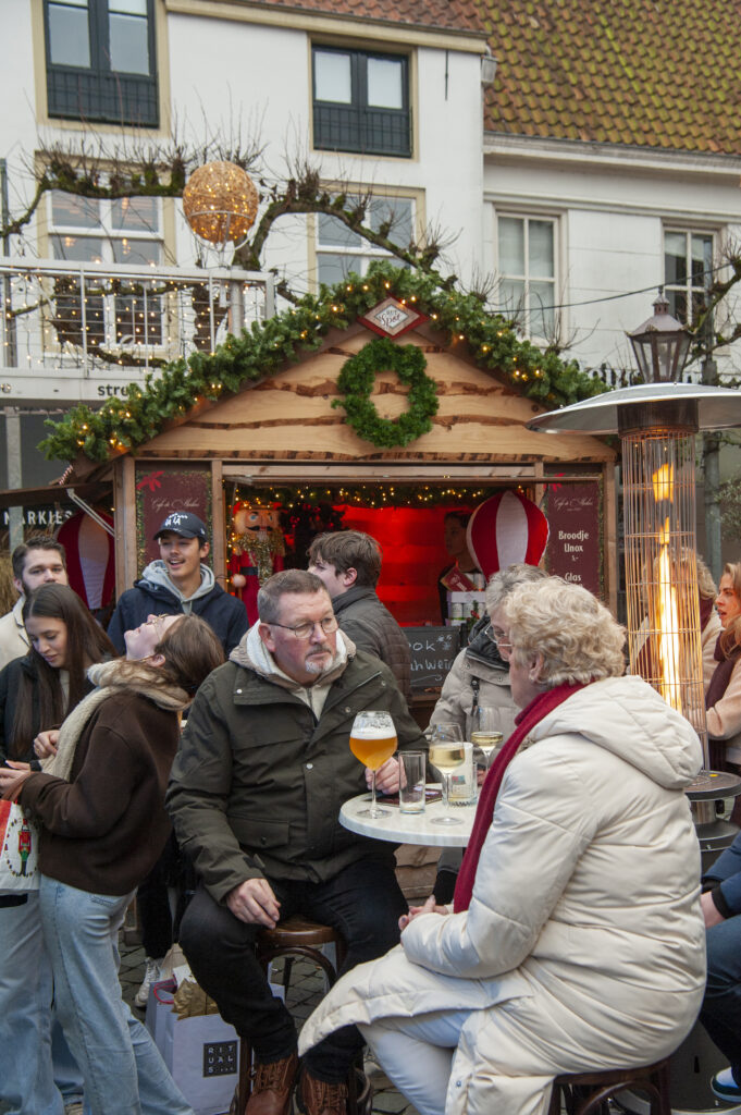 Mensen genieten van een wintermarkt met versierde kraampjes warme dranken en sfeerverlichting in een gezellige stedelijke omgeving met feestelijke decoraties